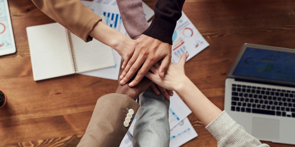 Team members stack hands above project meeting table